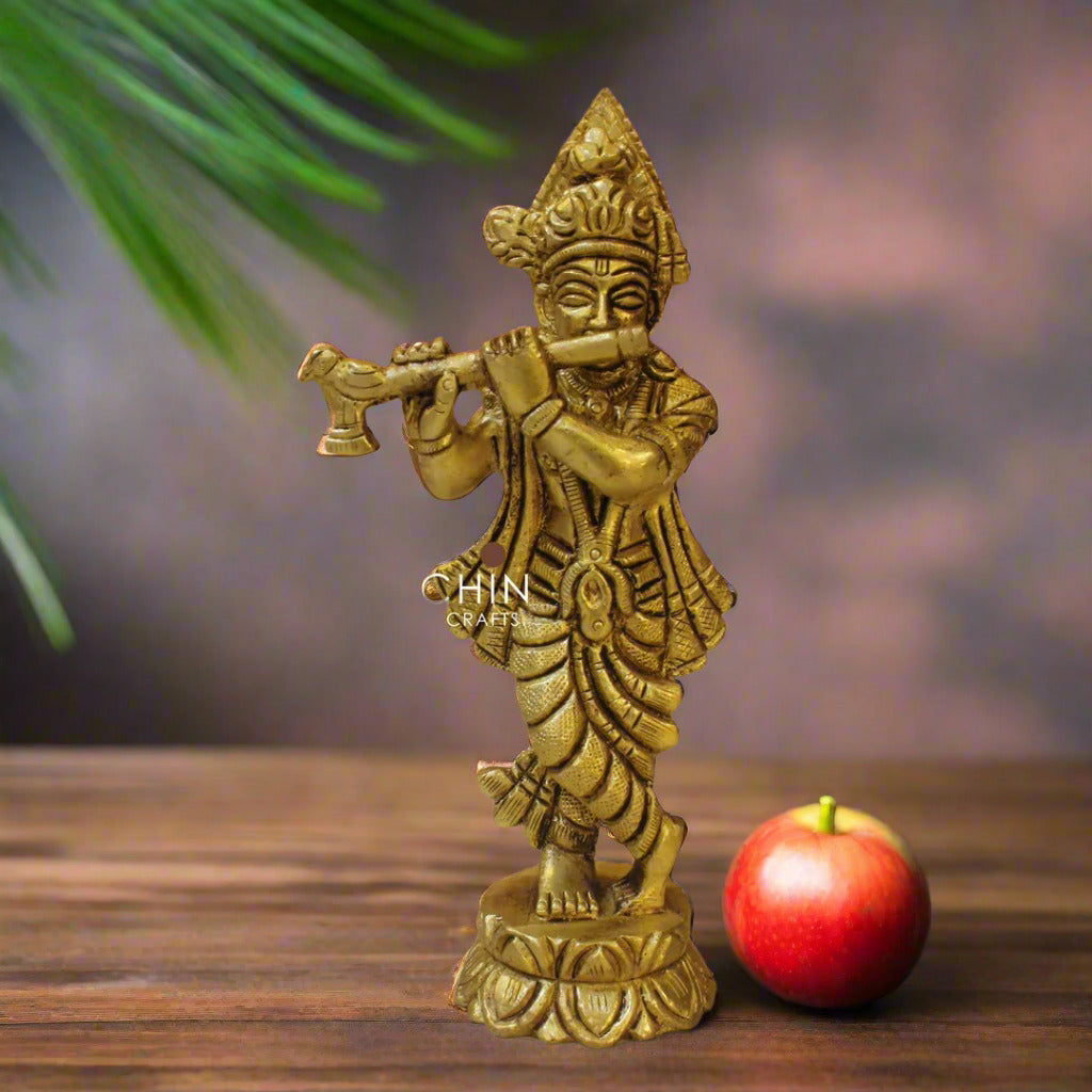 Gold-colored statue of a deity playing a flute on a wooden surface with 'Prachin Art & Crafts' branding.